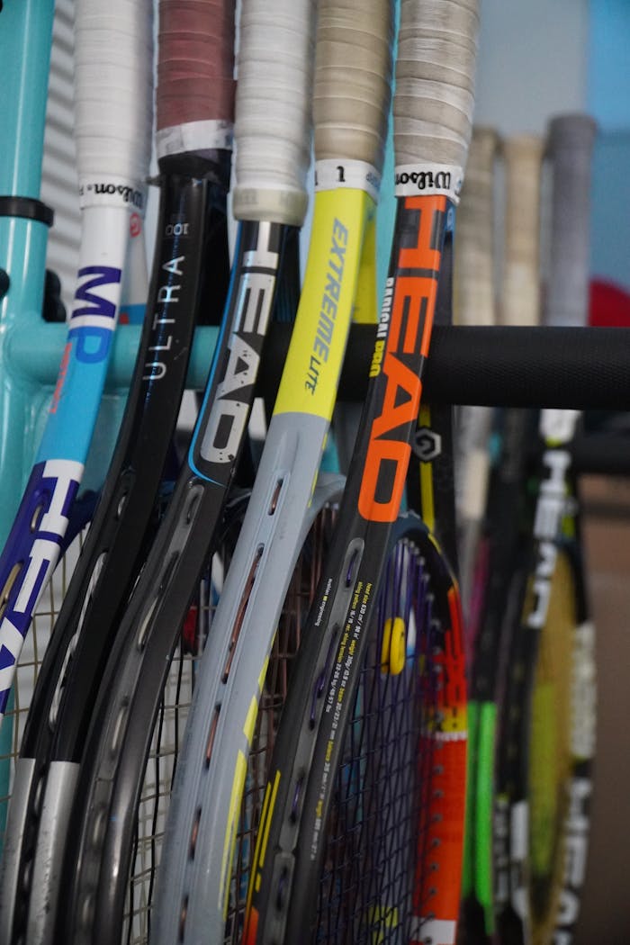 A close-up of various tennis rackets stacked closely together indoors.
