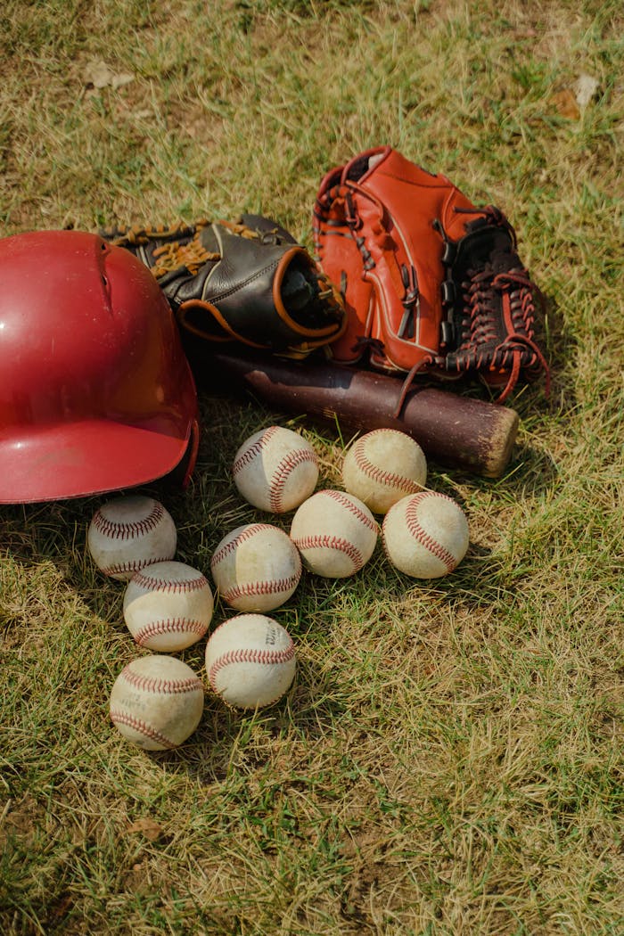 Baseball gear including balls, gloves, bat, and helmet arranged on grass.